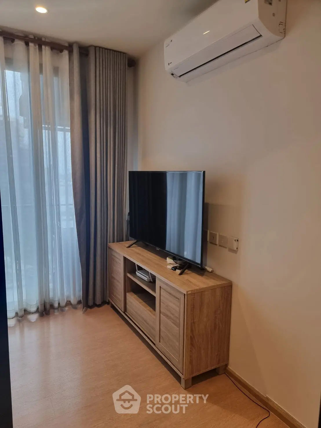 Modern living room with TV and air conditioning, featuring floor-to-ceiling windows and elegant curtains.