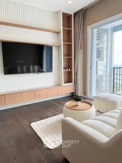 Modern living room with stylish furniture and large TV, featuring a cozy balcony view.