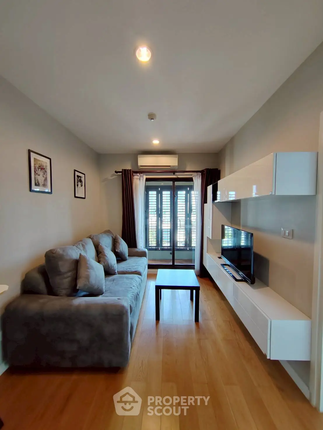 Modern living room with cozy sofa and wall-mounted TV, featuring wooden flooring and balcony access.