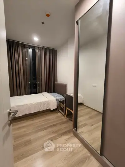 Modern bedroom with sleek design, featuring a large mirror and floor-to-ceiling window with city view.