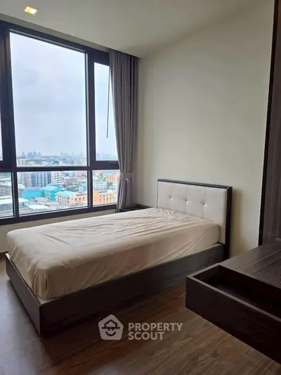 Modern bedroom with large window offering stunning city views, featuring sleek furniture and elegant design.