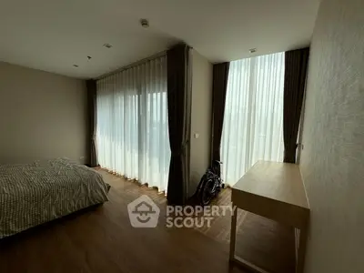 Spacious bedroom with large windows and natural light, featuring a minimalist design and wooden flooring.