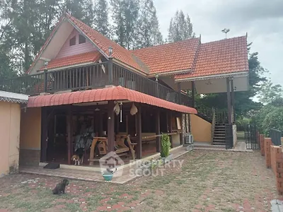 Charming traditional-style home with terracotta roof tiles, expansive paved courtyard, and a cozy outdoor seating area under a covered porch, surrounded by lush greenery.