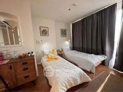 Cozy bedroom with twin beds, wooden flooring, and natural light, perfect for a comfortable stay.