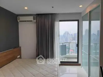 Modern bedroom with city view and balcony access in high-rise apartment.