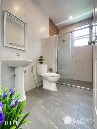 Modern bathroom with sleek finishes, featuring a glass-enclosed shower, pedestal sink, and tiled flooring, perfect for a contemporary home.