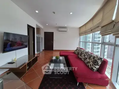 Spacious living room with modern red sofa and large windows offering city views.