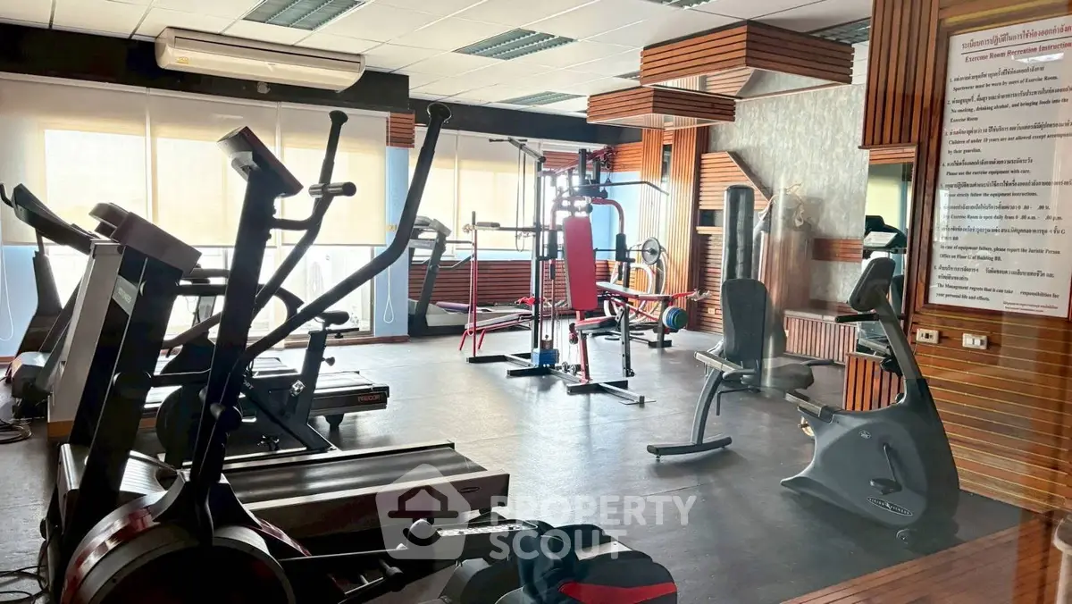 Spacious gym with modern fitness equipment and large windows for natural light.