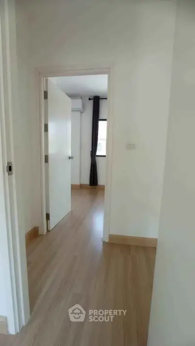 Bright hallway leading to a cozy bedroom with wooden flooring and natural light.