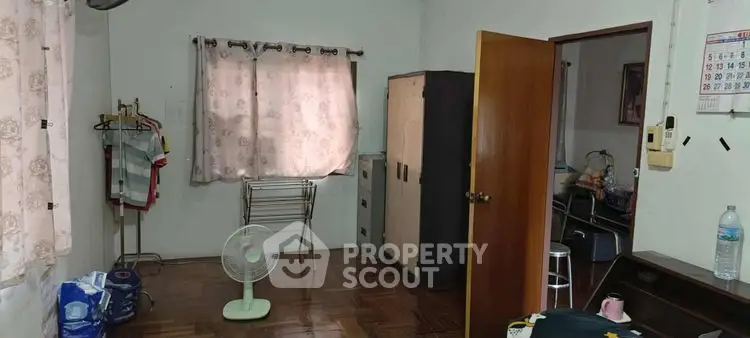Cozy bedroom with wooden flooring, wardrobe, and natural light through curtains.