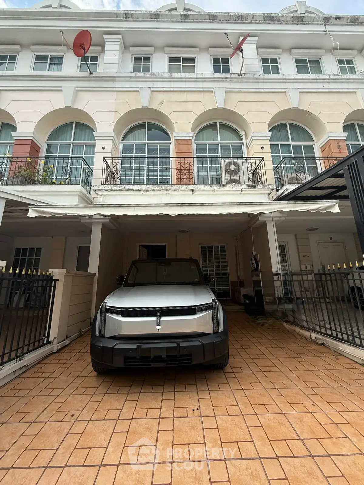 Elegant townhouse with spacious driveway and modern vehicle parked, showcasing classic architecture and balcony views.
