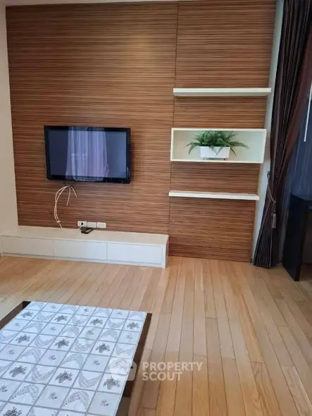 Modern living room with wooden flooring and wall-mounted TV, featuring stylish shelves.