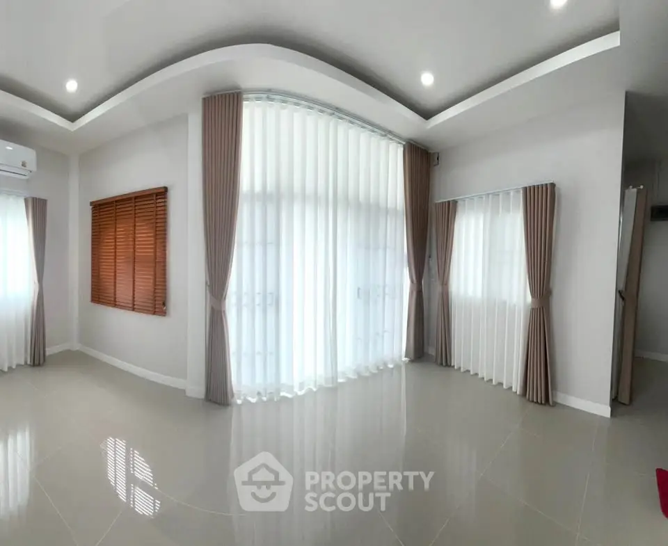 Spacious living room with large windows and elegant curtains, perfect for natural light and modern living.