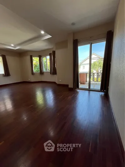 Spacious living room with hardwood floors and large windows offering natural light and garden view.