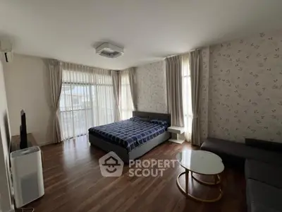 Spacious and well-lit bedroom with polished hardwood floors, large windows draped with elegant curtains, and modern furnishings including a king-sized bed and a cozy seating area.