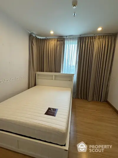 Cozy bedroom with wooden flooring and elegant curtains, perfect for relaxation.