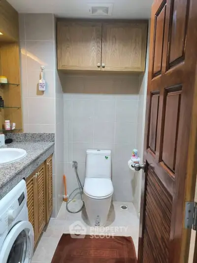 Cozy bathroom with modern amenities and washing machine, featuring wooden cabinets and granite countertop.
