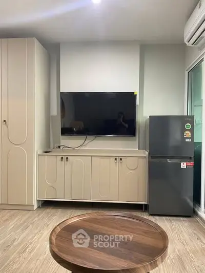 Modern living room with sleek cabinetry and flat-screen TV, featuring a compact fridge and stylish round table.