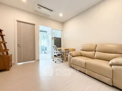 Modern living room with beige leather sofa and study area, perfect for relaxation and work.