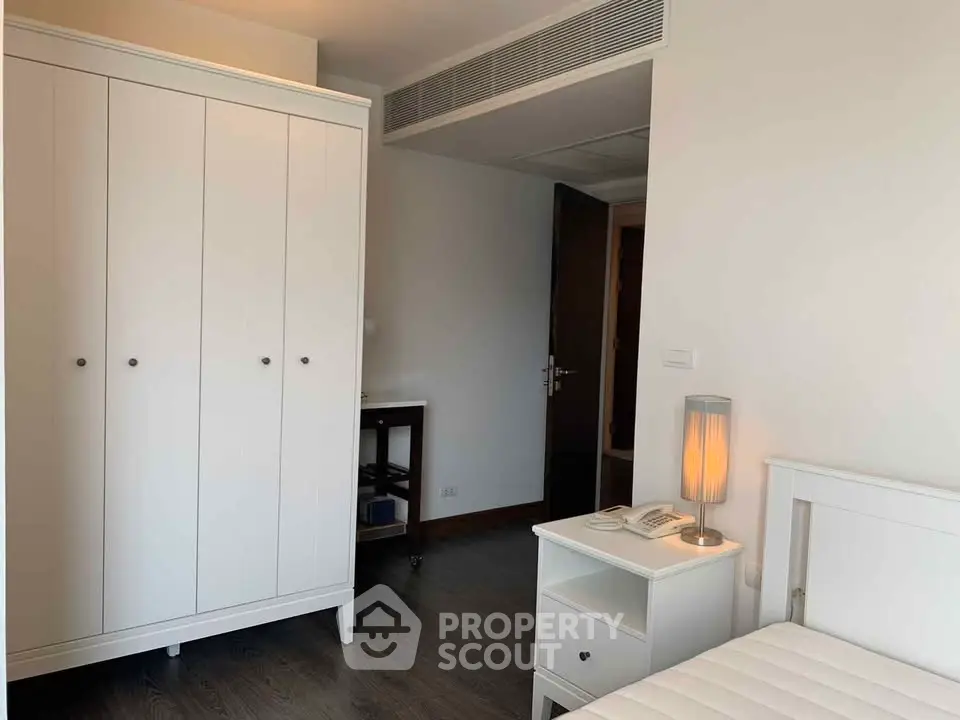 Modern bedroom with white furniture and sleek design, featuring a wardrobe and bedside table with lamp.