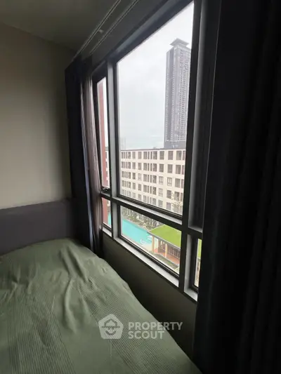 Cozy bedroom with large window offering stunning cityscape and pool view, perfect for urban living.