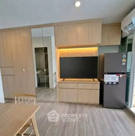 Modern living room with sleek wooden cabinetry and integrated TV unit, featuring a stylish dining area and refrigerator.