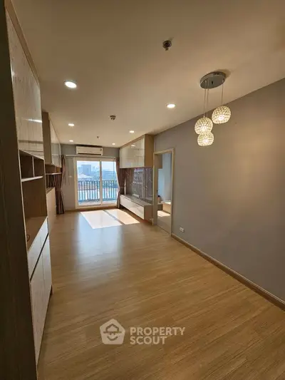 Spacious modern living room with wooden flooring and stylish lighting, featuring a large window with city view.