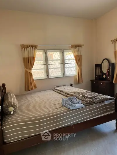 Cozy bedroom with natural light, featuring a comfortable bed and elegant curtains, perfect for relaxation.