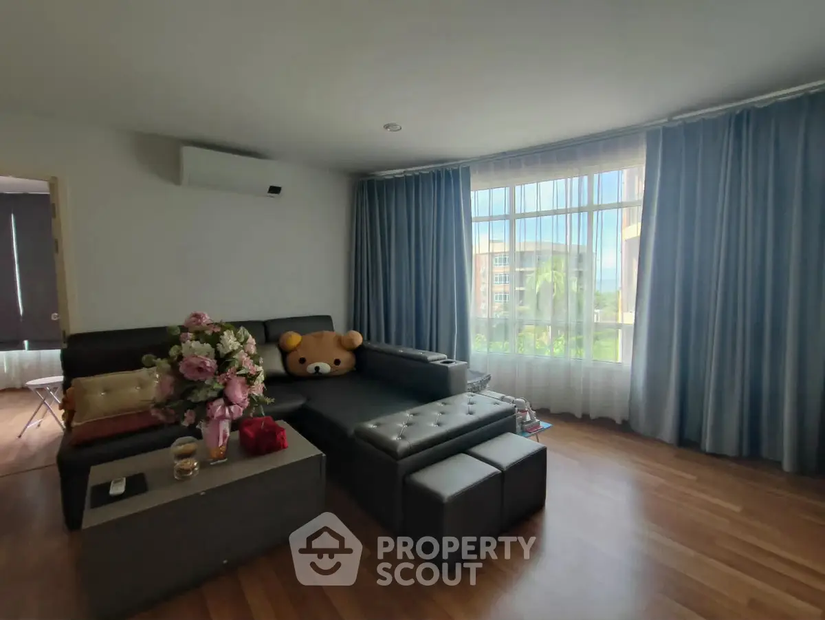 Spacious living room with large windows and modern decor, featuring a plush sofa and elegant curtains.