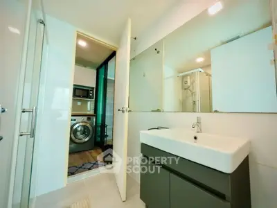 Modern bathroom with sleek sink and view into laundry area with washing machine.