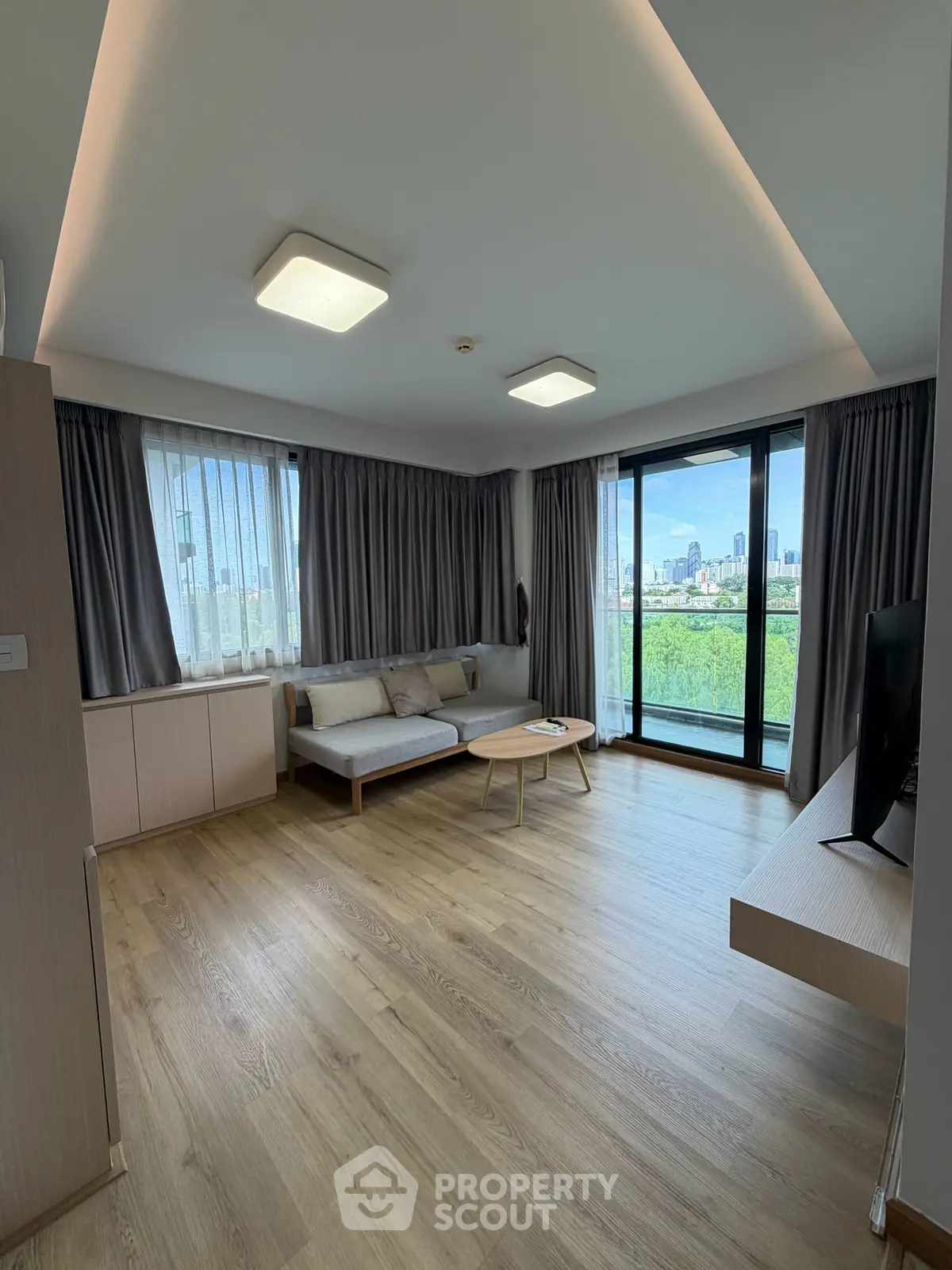 Spacious modern living room with large windows and city view, featuring sleek wooden flooring and contemporary furniture.
