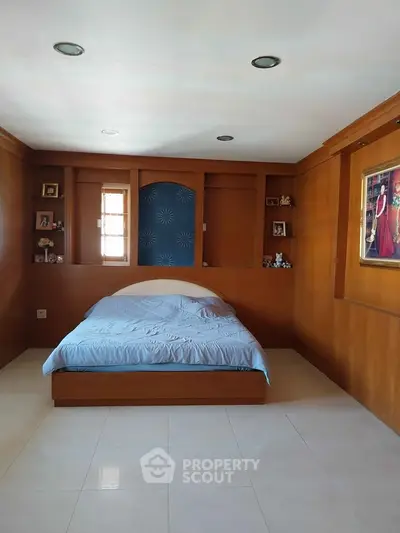 Spacious bedroom with wooden paneling and built-in shelves, featuring a cozy bed and elegant decor.