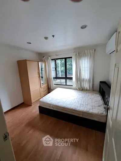 Spacious bedroom with wooden flooring and large window for natural light.