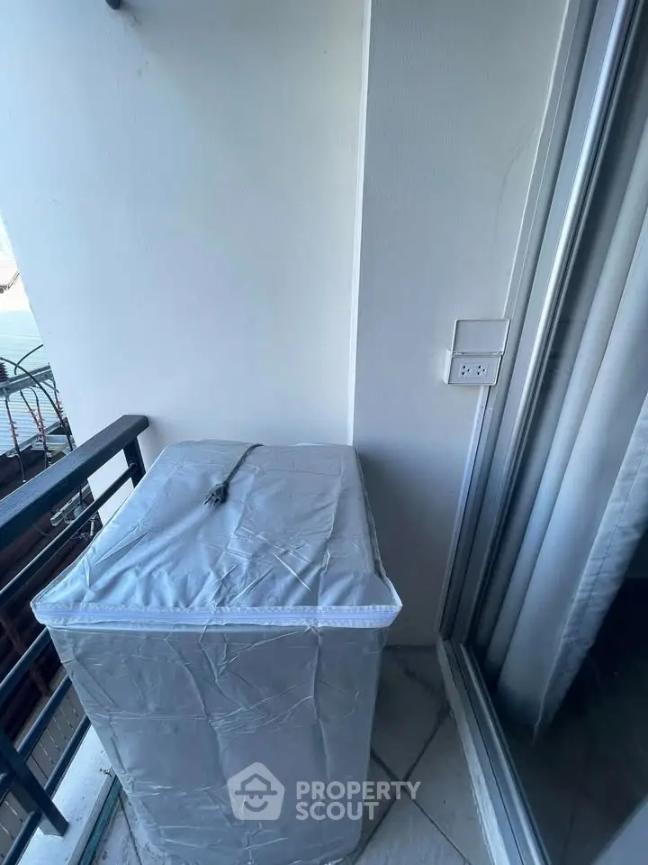 Compact balcony with covered appliance and railing, ideal for urban living.