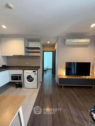 Modern apartment interior with open kitchen and living area featuring washing machine and TV.