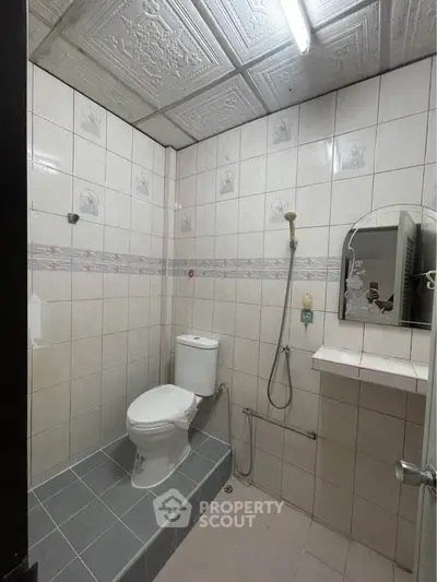 Compact bathroom with tiled walls, toilet, and shower area in a real estate property.