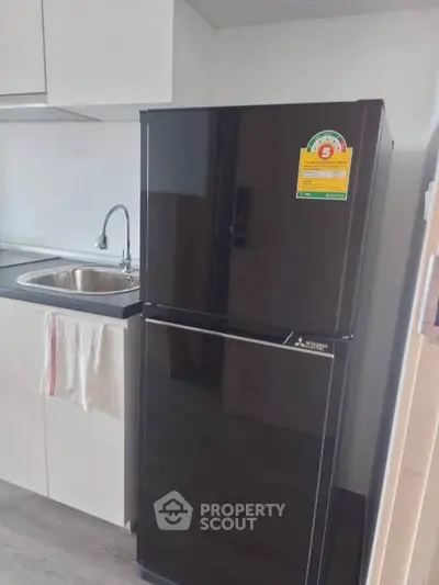 Modern kitchen with sleek black refrigerator and stainless steel sink, perfect for contemporary living.