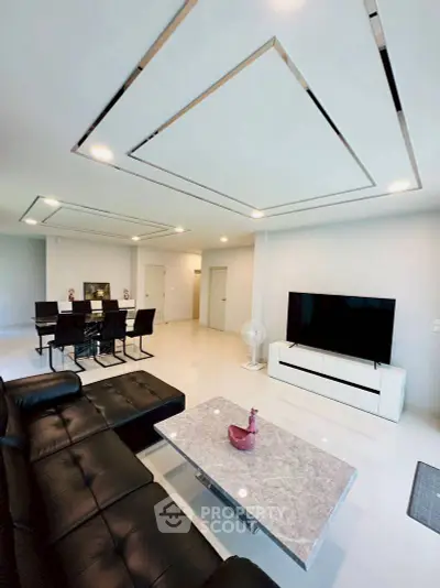 Modern living room with sleek black leather sofa, marble coffee table, and large flat-screen TV.