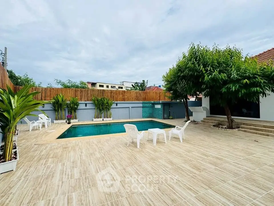 Spacious outdoor pool area with seating and lush greenery, perfect for relaxation.