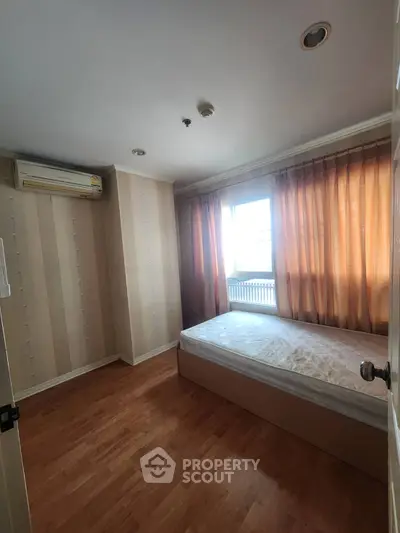 Cozy bedroom with natural light and wooden flooring, featuring a single bed and air conditioning.