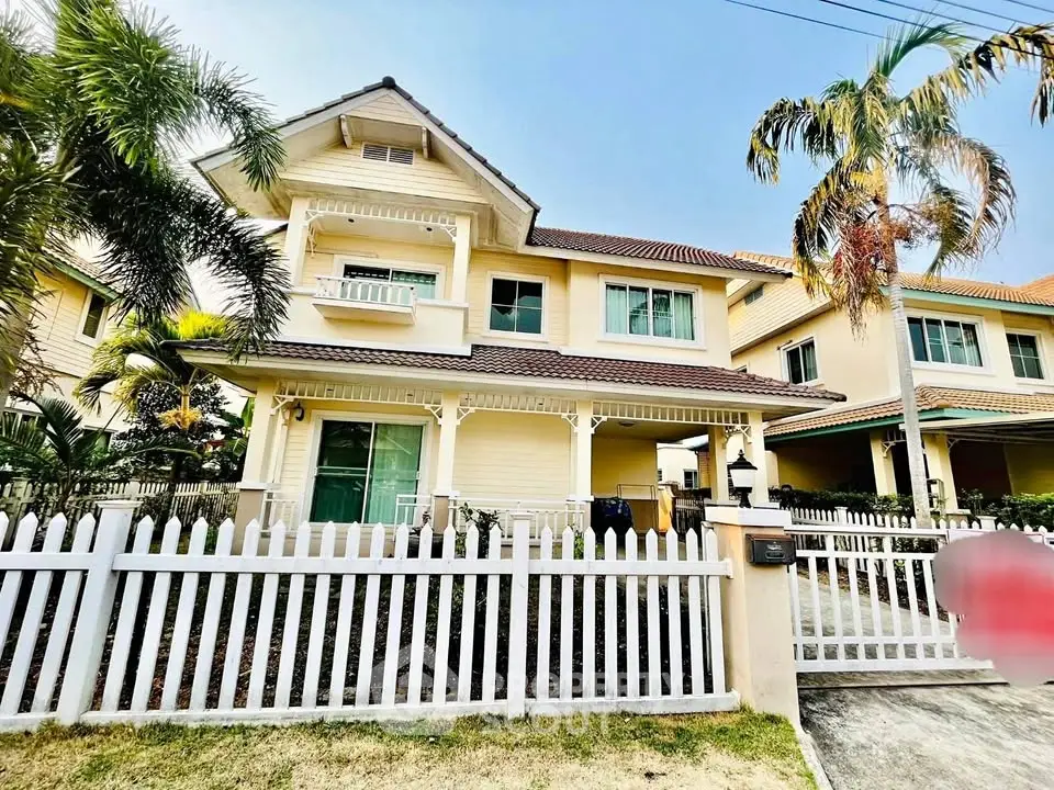 Charming two-story house with white picket fence and lush palm trees