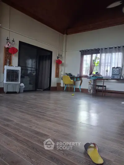 Spacious living room with wooden flooring and high ceiling, featuring a cozy workspace and modern decor.