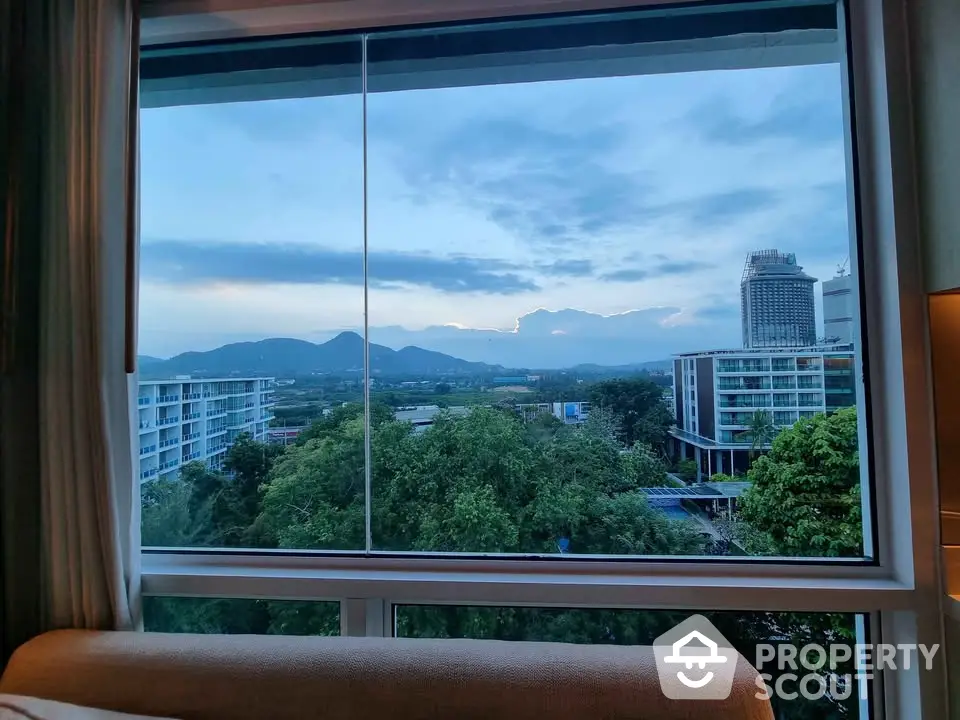 Stunning view from window overlooking lush greenery and cityscape with mountains in the background.