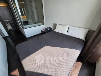 Modern bedroom with glass-walled ensuite bathroom and sleek dark flooring.