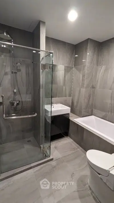 Modern bathroom with glass shower and bathtub in sleek gray tiles