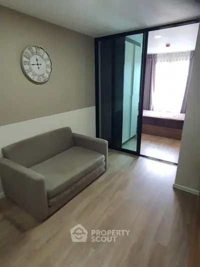 Cozy small living area with sofa and clock, leading to a bright bedroom.