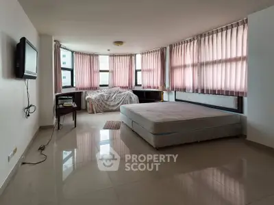 Spacious bedroom with large windows and natural light, featuring a minimalist setup and tiled flooring.