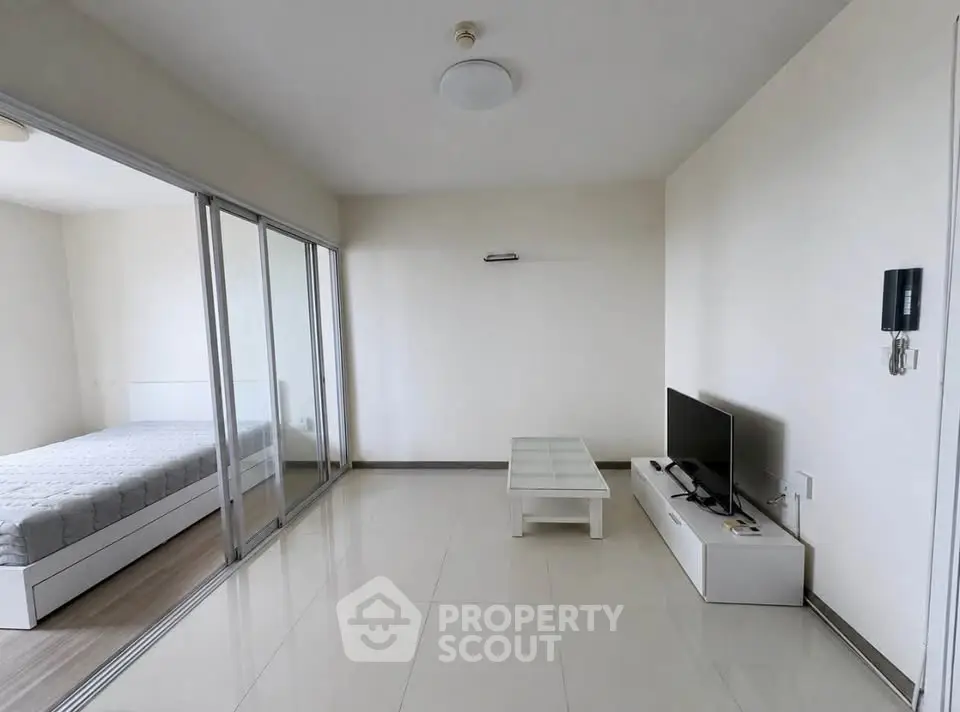 Modern living room with glass partition to bedroom, sleek TV setup, and minimalist decor.