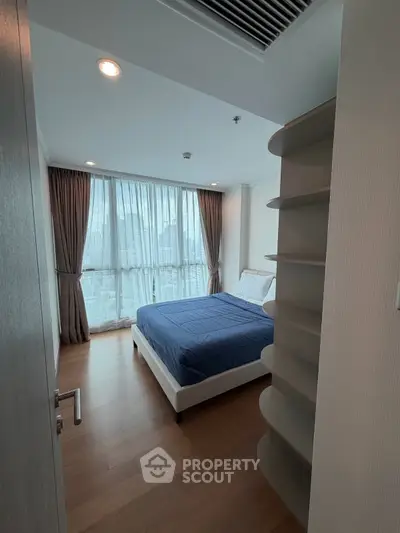 Modern bedroom with large window and city view, featuring sleek wooden flooring and stylish curtains.