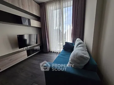 Modern living room with sleek TV setup and cozy blue sofa, featuring floor-to-ceiling windows for natural light.